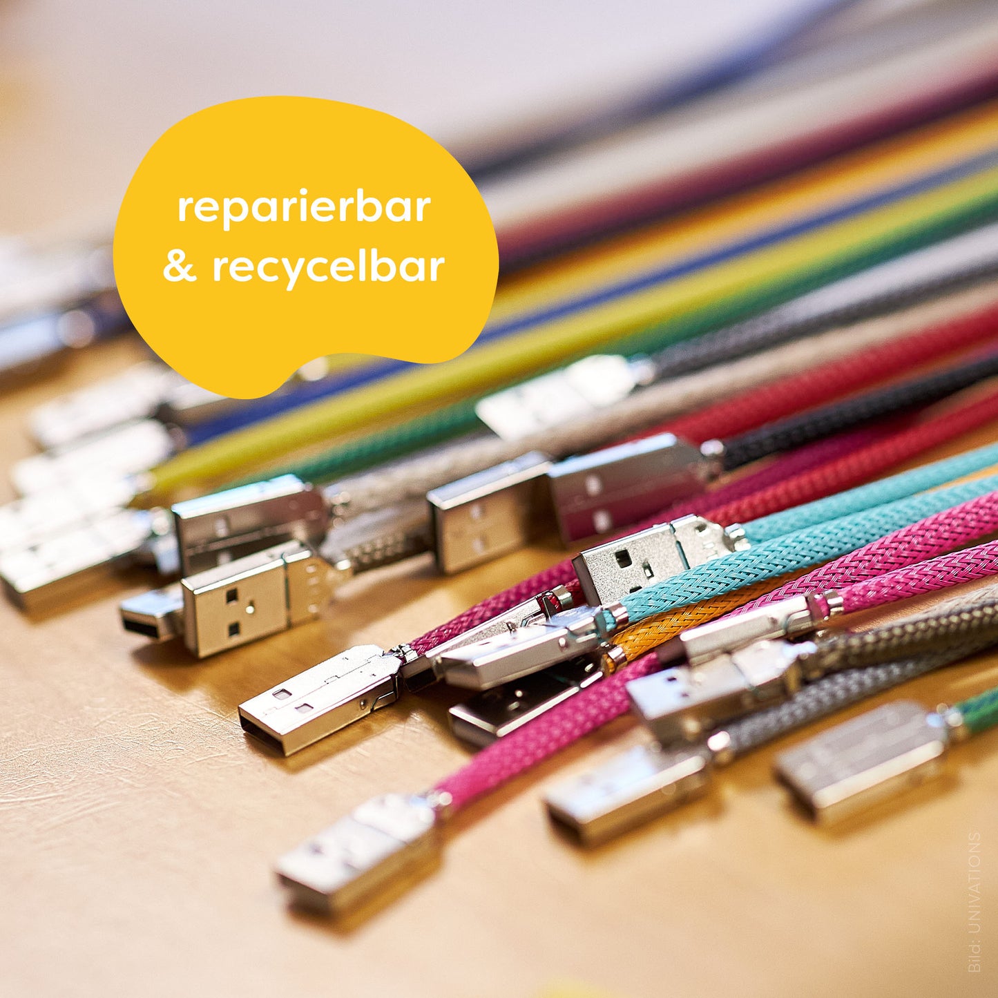 recable is repairable & recyclable. Illustration: Numerous colorful recable with USB-A connectors without heat shrink tubing lie on a wooden table.